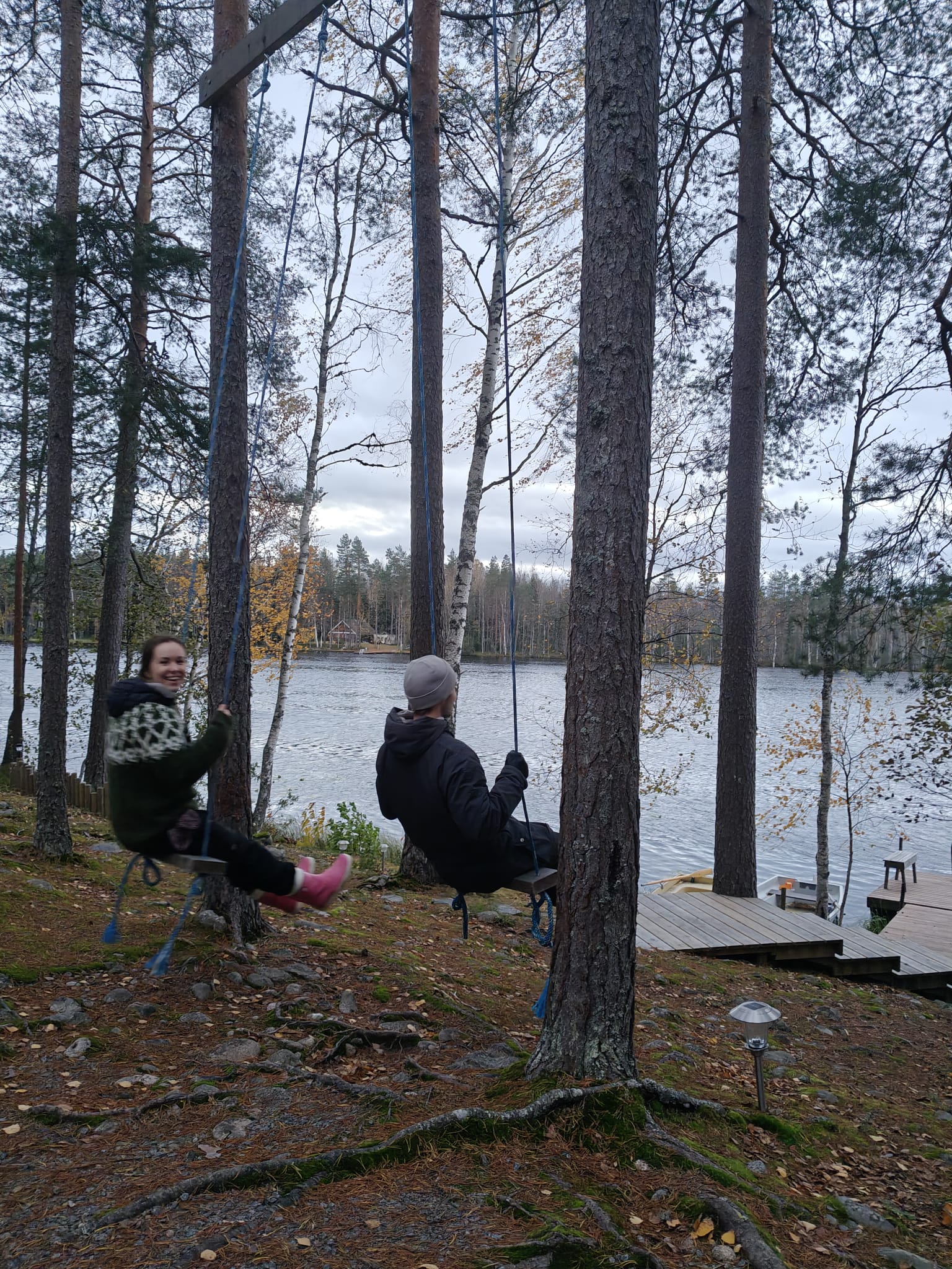 kaksi henkilöä keinuu järven rannalla